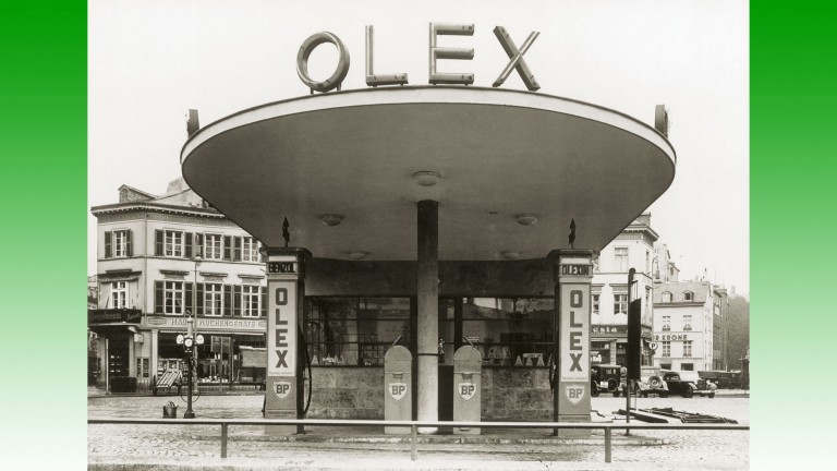 Station essence Olex avec pompes en bordure de route, située dans un centre-ville allemand dans les années 1920.
